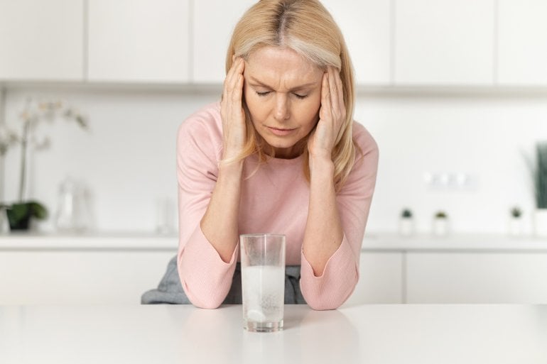 Frau nimmt eine Brausetablette mit Aspirin, weil sie Kopfschmerzen hat