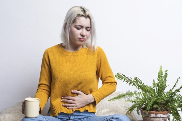 Frau trinkt eine Tasse Tee und hält sich den Bauch, weil sie Blähungen hat