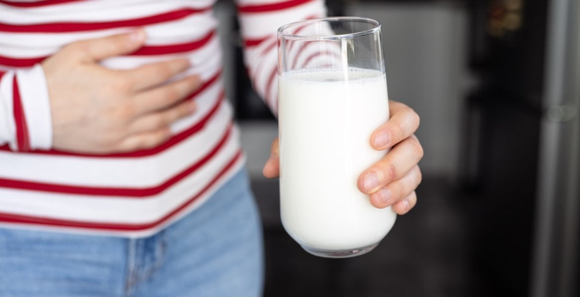 Frau mit Laktoseintoleranz hält ein Glas Milch und eine Hand auf ihren Bauch