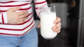 Frau mit Laktoseintoleranz hält ein Glas Milch und eine Hand auf ihren Bauch