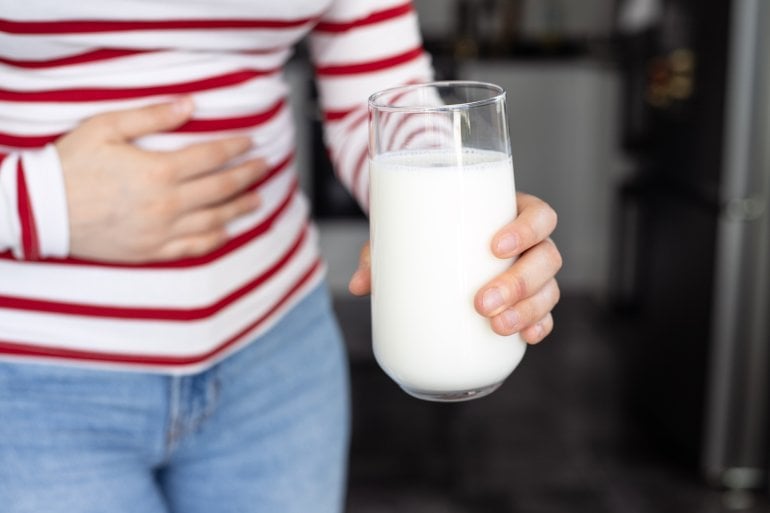 Frau mit Laktoseintoleranz hält ein Glas Milch und eine Hand auf ihren Bauch