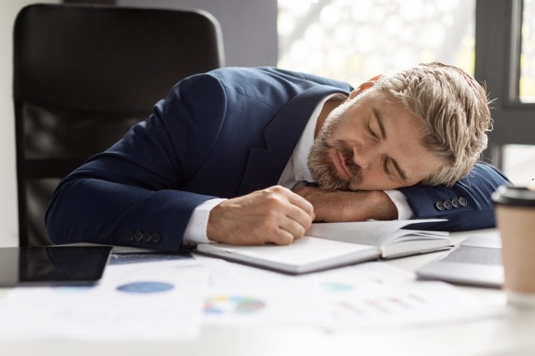 Mann mit Narkolepsie schläft am Schreibtisch