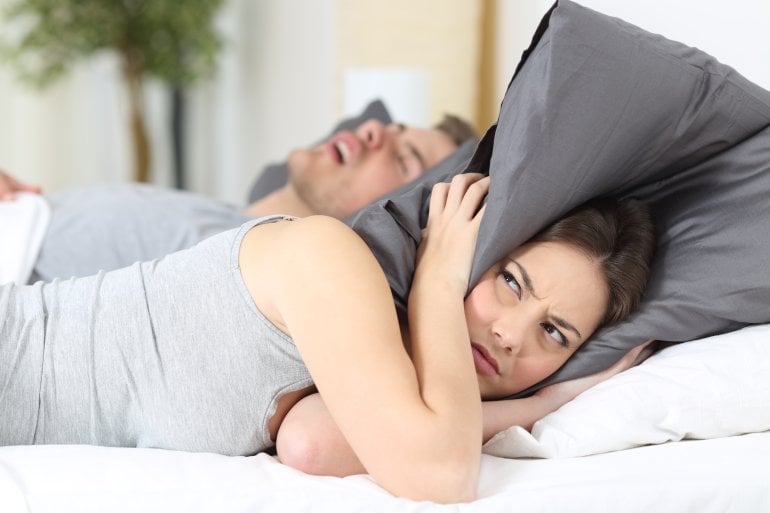 Frau mit schnarchendem Mann hält Kissen über Ohren