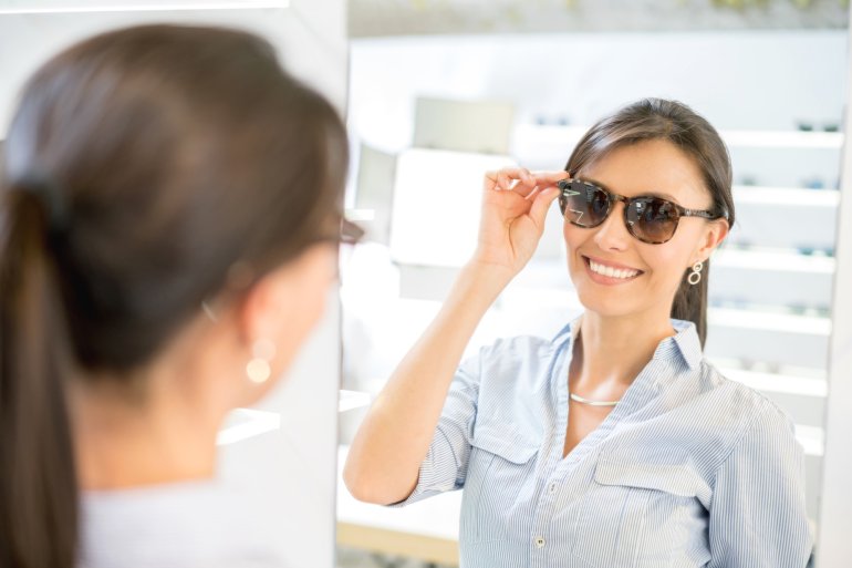 Frau probiert vor dem Spiegel eine Sonnenbrille auf