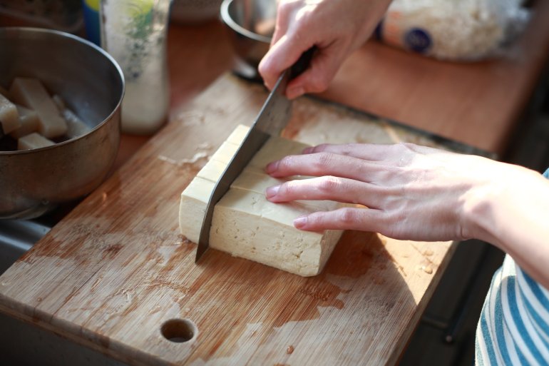 Frau schneidet Tofu auf einem Brettchen