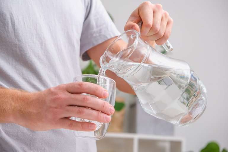 Mann schenkt sich Wasser in ein Glas ein